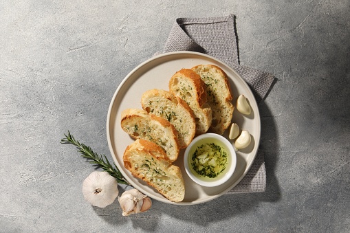 Tasty baguette with garlic and dill served on grey textured table, top view