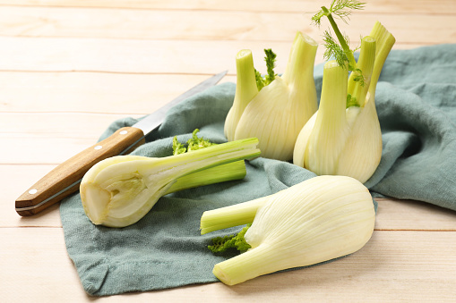Fresh raw fennel bulbs and knife on light wooden table