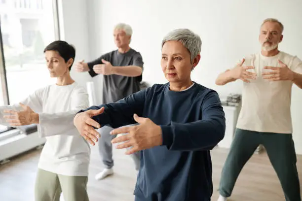 Medium full shot of senior male and female qigong class participants practicing tree pose for meditation