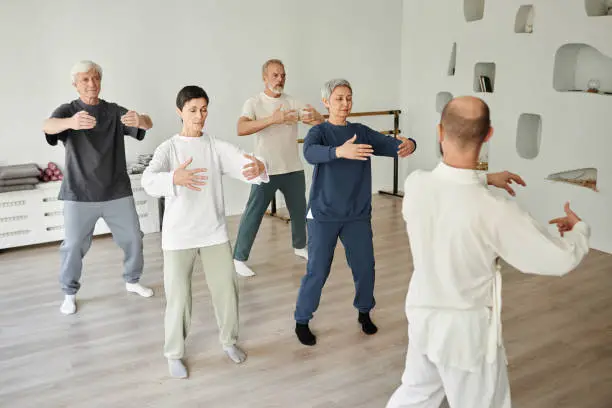 Wide shot of senior people meditating during qigong exercise in fitness studio while male instructor teaching