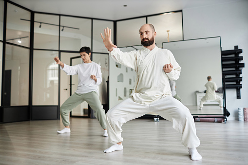 Full shot of qigong instructor in white outfit and female student doing energy concentration exercise