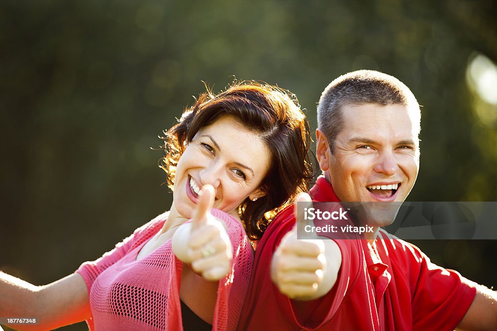 Happy couple outdoor portrait Portrait of a happy smiling couple at the park, sitting back to back, showing thumbs up 30-39 Years Stock Photo