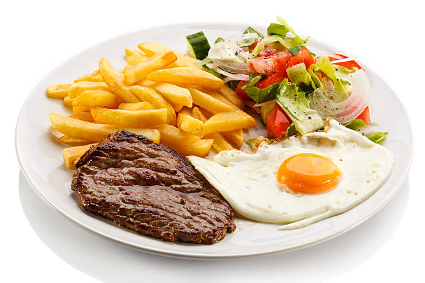 Beefsteak, fried egg, French fries and vegetables