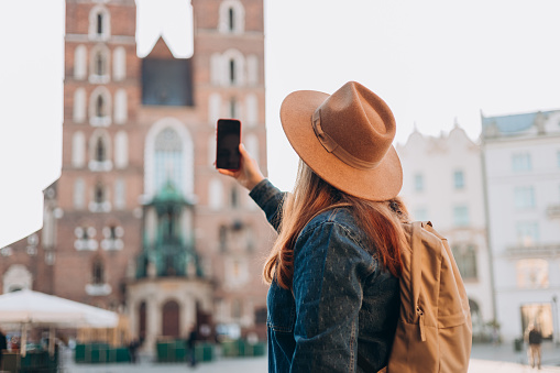 Feliz joven turista europeo con mochila en sombrero hace una foto o un video en el teléfono inteligente en la Plaza del Mercado en Cracovia. Viajar por Europa en verano. Basílica de Santa María. Concepto vacacional photo