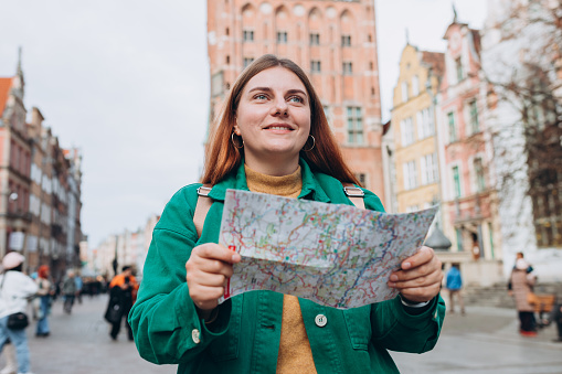 Portrait beautiful woman with paper map in street. Happy tourist travels in Europe. Vacation concept by exploring interesting places to travel. Women Searching locations at autumn day.