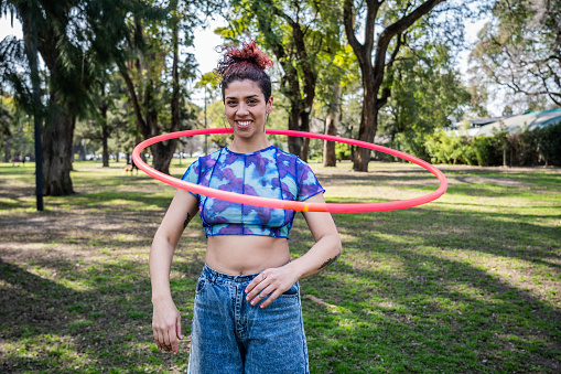 Portrait of a young woman juggling with hula hoop at public park