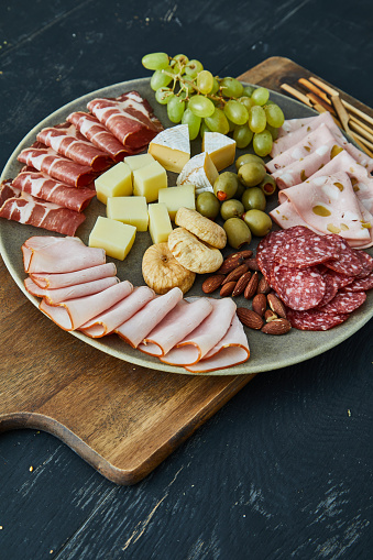 Charcuterie dark mood luxury. A perfect holiday appetizer plate, made from variety of ham and cheese delicatessen, dry beef ham, dry pork sausage, Camembert cheese, Gauda cheese, organic olives, dry figs, cherry tomato, rosemary, fresh olive oil, local organic seasoning, herbs and spices. Representing a healthy lifestyle, healthy eating, a wellbeing, modern city life, traditional culture and a perfect brunch gourmet delicatessen.