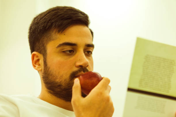 istock The young man with a beard reading a book and eating an apple at home. 1877818229