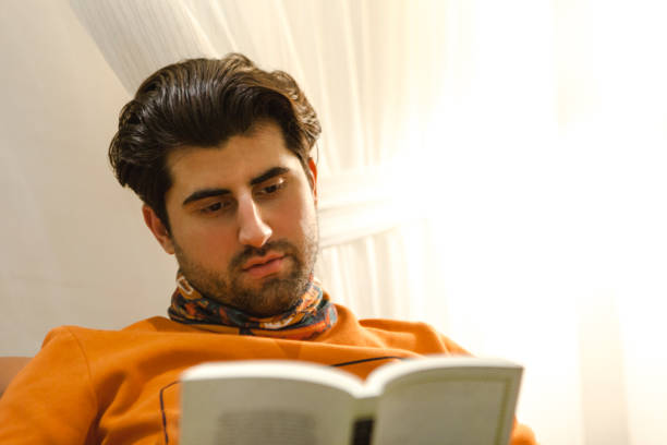 istock Young handsome guy reading a novel at home. 1877820292