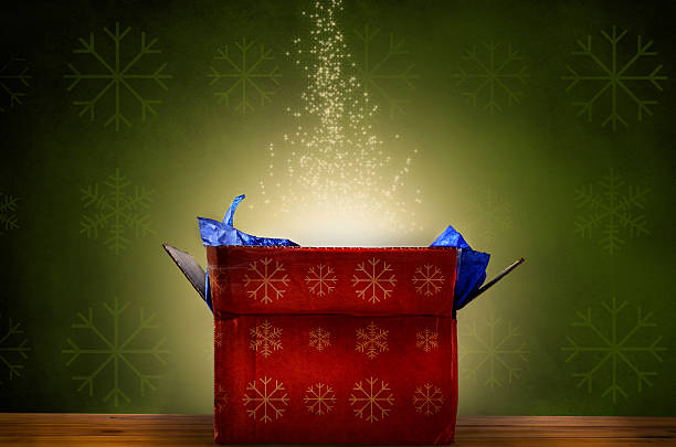 Opened Christmas Gift Box with Glow and Sparkling Stars An opened red Christmas gift box with gold snowflake patterns, emitting a magical warm bright glowing light and rising sparkling stars.  Set against a green patterned fabric wallpaper effect on a wooden planked surface. emitting stock pictures, royalty-free photos & images