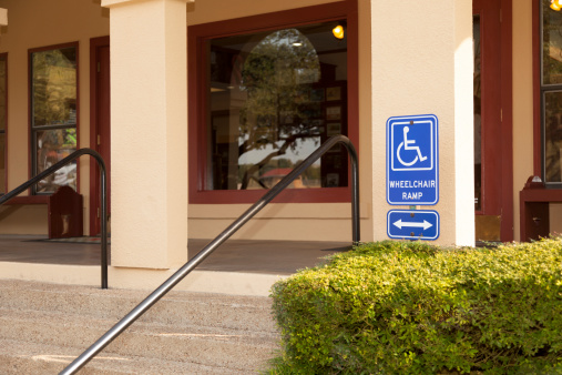 Wheelchair ramp sign posted on building entrance. Stairs and porch of commercial building.
