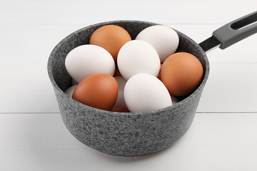 Unpeeled boiled eggs in saucepan on white wooden table, closeup