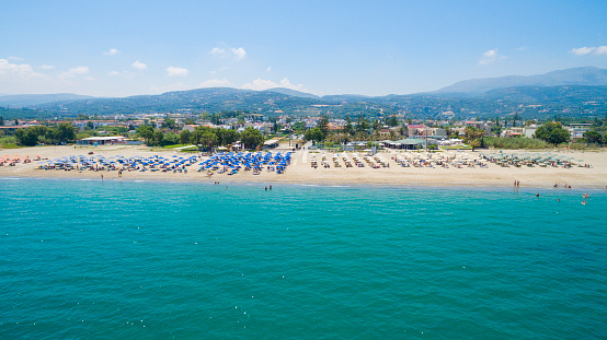 View on sand beach and turquoise sea shore at Agios Georgios Pagon at Corfu island, Greece with beatiful blooming pink Nerium oleander, aloe vera plant and couple relaxing on sunbed with white umbrella, green hill and clear blue sky backgound.