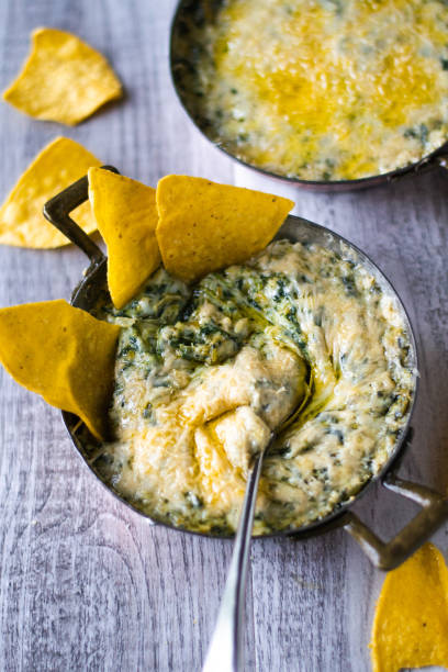 istock Spinach and Artichoke Dip with Tortilla Chips sticking out and a silver spoon placed inside resting to the front. 1877873461