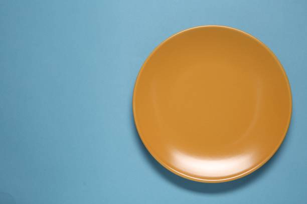 istock One orange ceramic plate on light blue background, top view. Space for text 1877878810