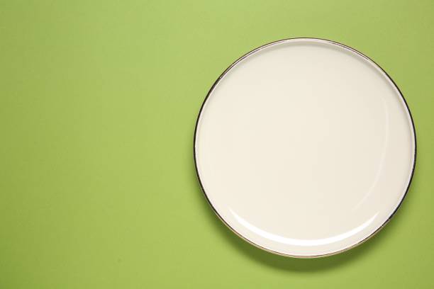 istock One white plate on green background, top view. Space for text 1877882508