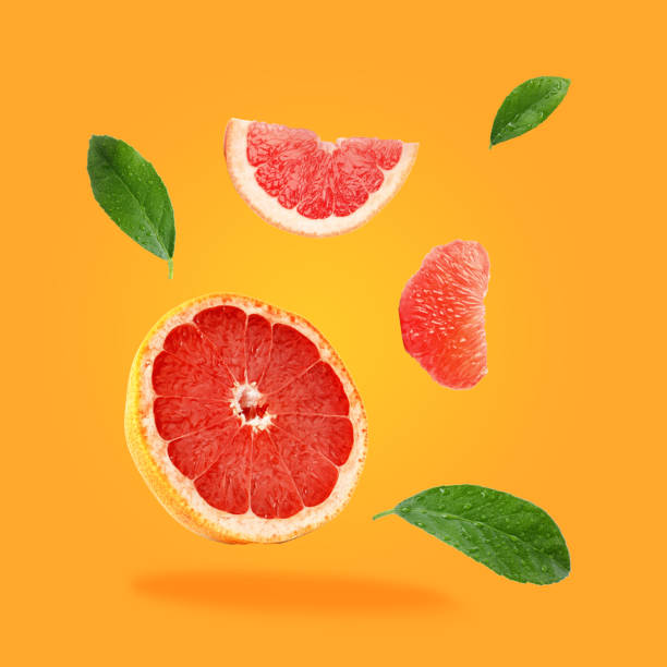 istock Pieces of grapefruit and green leaves falling on orange background 1877895343