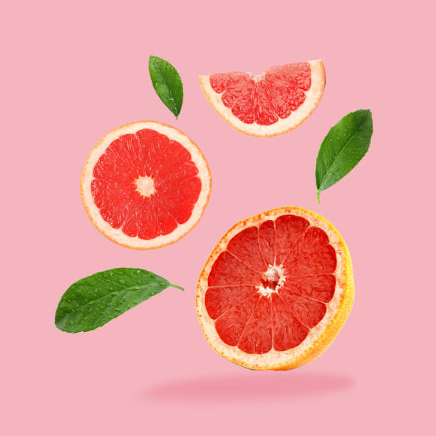 istock Pieces of grapefruit and green leaves falling on pink background 1877895346