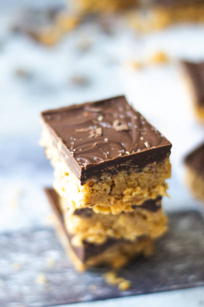 istock Side angle of Peanut Butter Scotcheroo's stacked and piled high on a blue grey distressed wooden background. 1877895348
