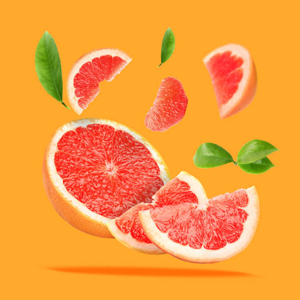istock Pieces of grapefruit and green leaves falling on orange background 1877895873