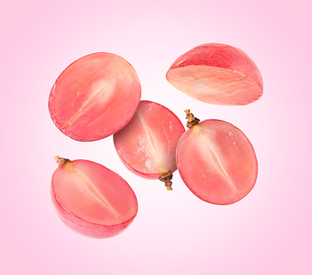 Halves of fresh grape falling on pink background