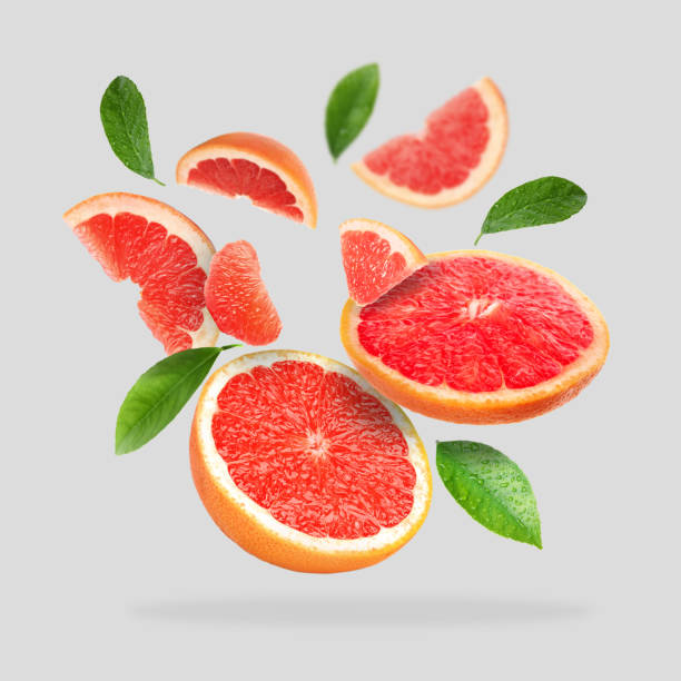 istock Pieces of grapefruit and green leaves falling on light gray background 1877897436