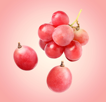 Many fresh grapes falling on pink background