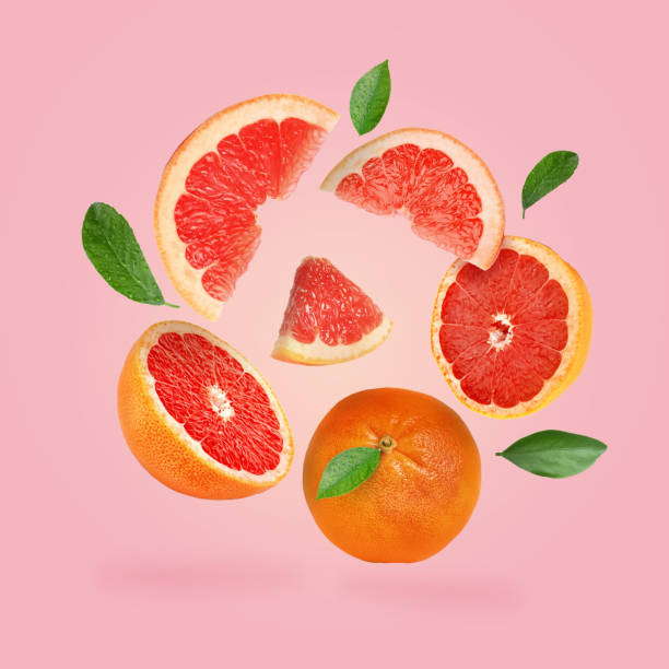 istock Cut and whole grapefruits and green leaves falling on pink background 1877899511