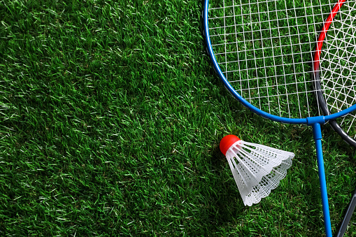 Two badminton rackets and shuttlecock on green grass, top view with space for text