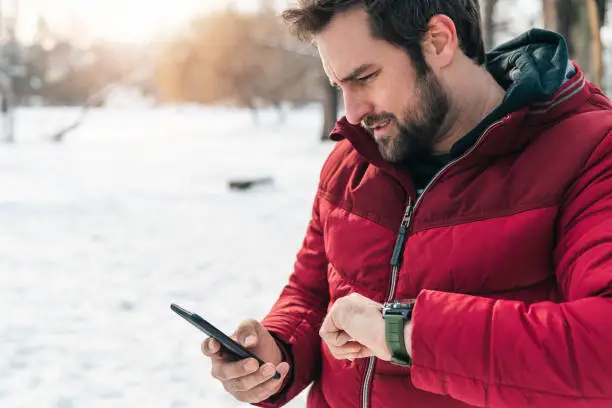 Photo of Serious man texting on mobile phone while waiting for someone outdoors in the winter time