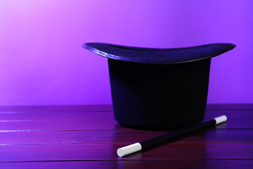 Black top hat and wand on wooden table, space for text. Magician equipment