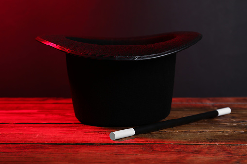 Black top hat and wand on wooden table. Magician equipment