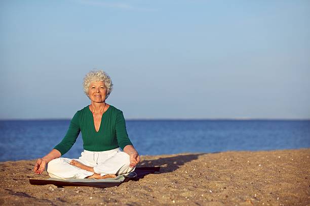 istock Senior woman meditating on beautiful beach 187809735