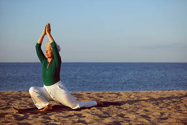 istock Senior woman practicing yoga on beach 187809740