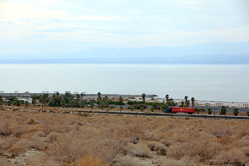 Large transport truck transporting goods  via highway 111 along the East shore of the Salton Sea California. Under the Salton Sea is one  of the largest Lithium deposits in the world.  View to the West side of the Salton Sea. Picnic tables located along shoreline. Not far from Palm Springs.