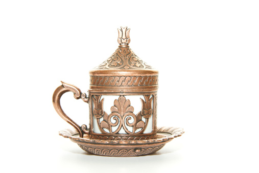 an old set of two white teapots and cups with a brown pattern stand on a gray table against a green wall