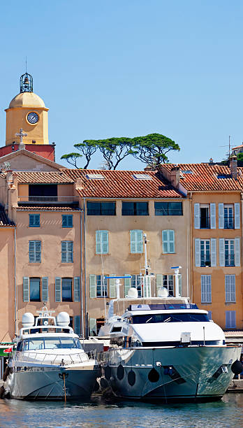 St Tropez Quayside The iconic view of St Tropez on the French Riviera, with luxury power boats moored at the quayside, pastel coloured houses, the tower of the church, Notre Dame of the Assumption, looming above the rooftops into a clear blue Mediterranean sky pierced by the distinctive mediterranean trees of the umbrella pine. Good copy space. pinus pinea photos stock pictures, royalty-free photos & images