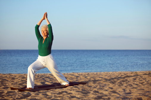 Mature woman stretching on the beach. Senior woman practicing yoga on the beach during morning