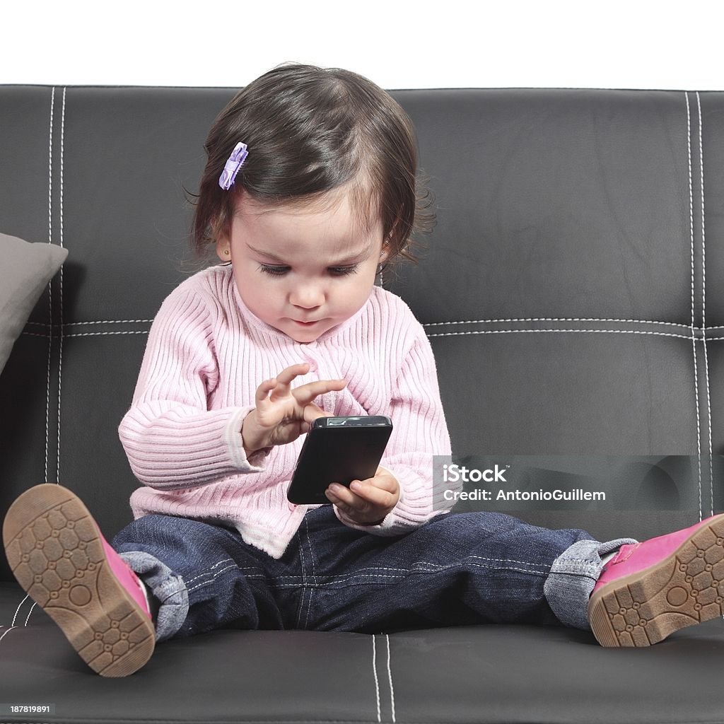 Cute baby browsing in a smartphone Cute baby browsing in a smartphone sitting on a black couch at home Adversity Stock Photo