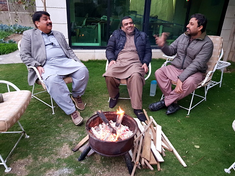 Three friends sitting on lawn chairs in warm dress with bonfire in winters.