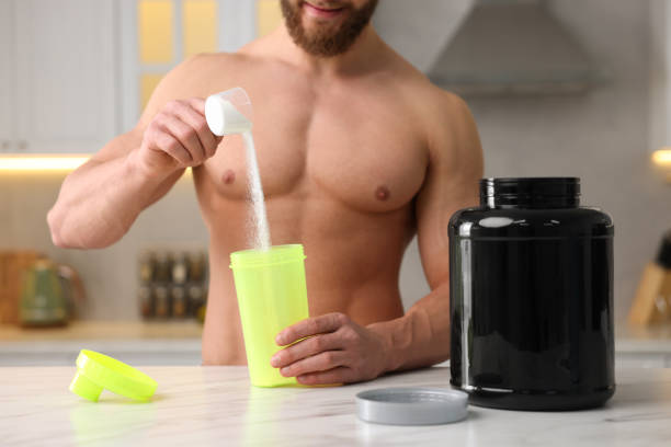 istock Young muscular man making protein shake at white marble table in kitchen, focus on jar 1878218065