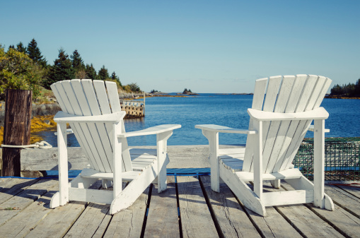 Two empty adirondack chairs sitting on a dock with an ocean view