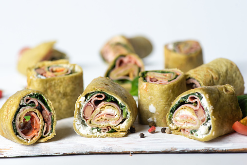 Tortilla rolls with spinach, cheese, ham and tomato on a white background
