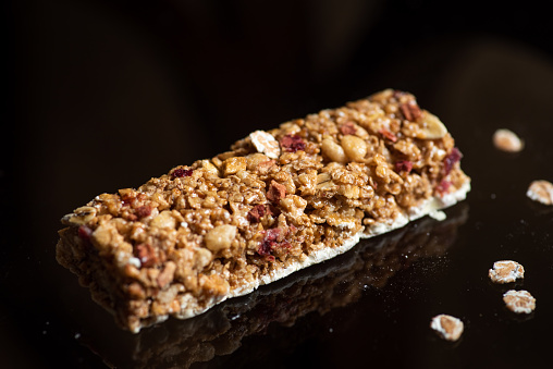 Protein energy bar with wholegrain cereals and cranberry fruit on glass table with reflection