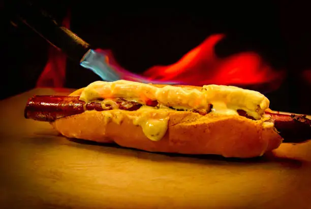 hot dog flambéed over strong flames, on top of a wooden table. Commercial scene