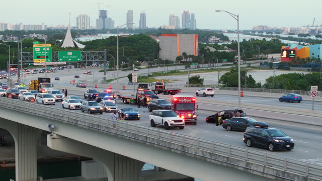 Emergency services and vehicles responding to accident site on American street in Miami, Florida. First responders helping victims of car crash on bridge road in the USA