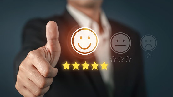 Businessman showing thumbs up to give five glowing golden stars and smile face icon for excellent on virtual touch screen,Customer service evaluation concept.