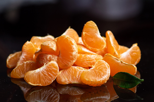 Heap of slices of tangerines on a dark glass table with reflection