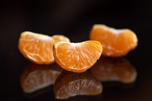 Slices of tangerines on a dark glass table, with reflection. Close up