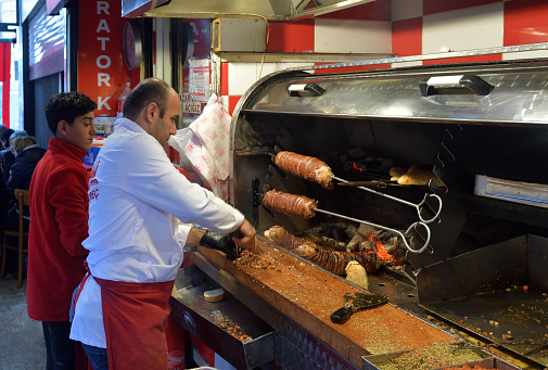 Istanbul, Turkey - December 11, 2023: Turkish man, kokorecci master chef cutting a skewer of meat for a Kokorec, or kokoretsi sandwich